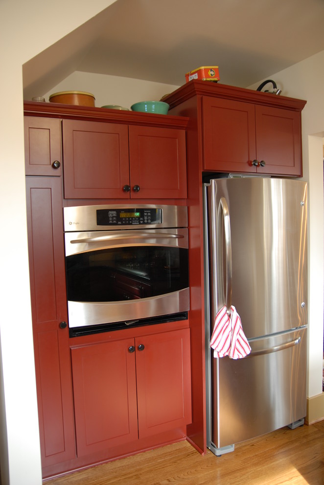 Mittelgroße Landhaus Küche mit Schrankfronten mit vertiefter Füllung, roten Schränken, Küchengeräten aus Edelstahl und hellem Holzboden in Sonstige