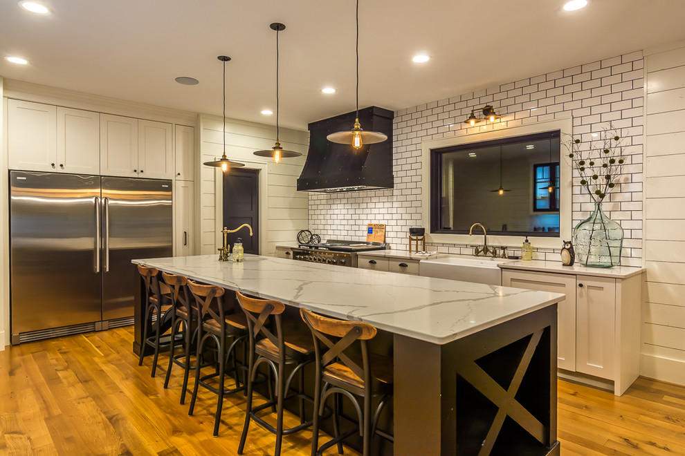 Inspiration for a large transitional galley medium tone wood floor eat-in kitchen remodel in Cedar Rapids with a farmhouse sink, shaker cabinets, beige cabinets, marble countertops, white backsplash, subway tile backsplash, stainless steel appliances and an island