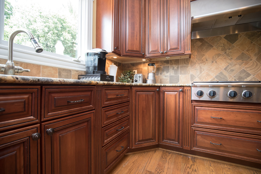 Mid-sized transitional u-shaped medium tone wood floor eat-in kitchen photo in DC Metro with an undermount sink, raised-panel cabinets, dark wood cabinets, granite countertops, beige backsplash, stone tile backsplash, stainless steel appliances and an island