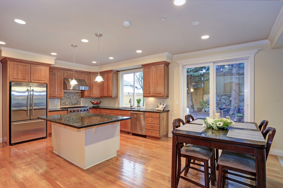 Inspiration for a mid-sized timeless l-shaped light wood floor and brown floor eat-in kitchen remodel in DC Metro with an undermount sink, raised-panel cabinets, brown cabinets, granite countertops, yellow backsplash, ceramic backsplash, stainless steel appliances, an island and green countertops