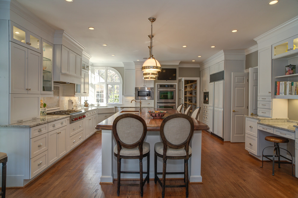 Photo of a large traditional u-shaped open plan kitchen in DC Metro with a submerged sink, shaker cabinets, white cabinets, wood worktops, white splashback, porcelain splashback, stainless steel appliances, dark hardwood flooring and an island.