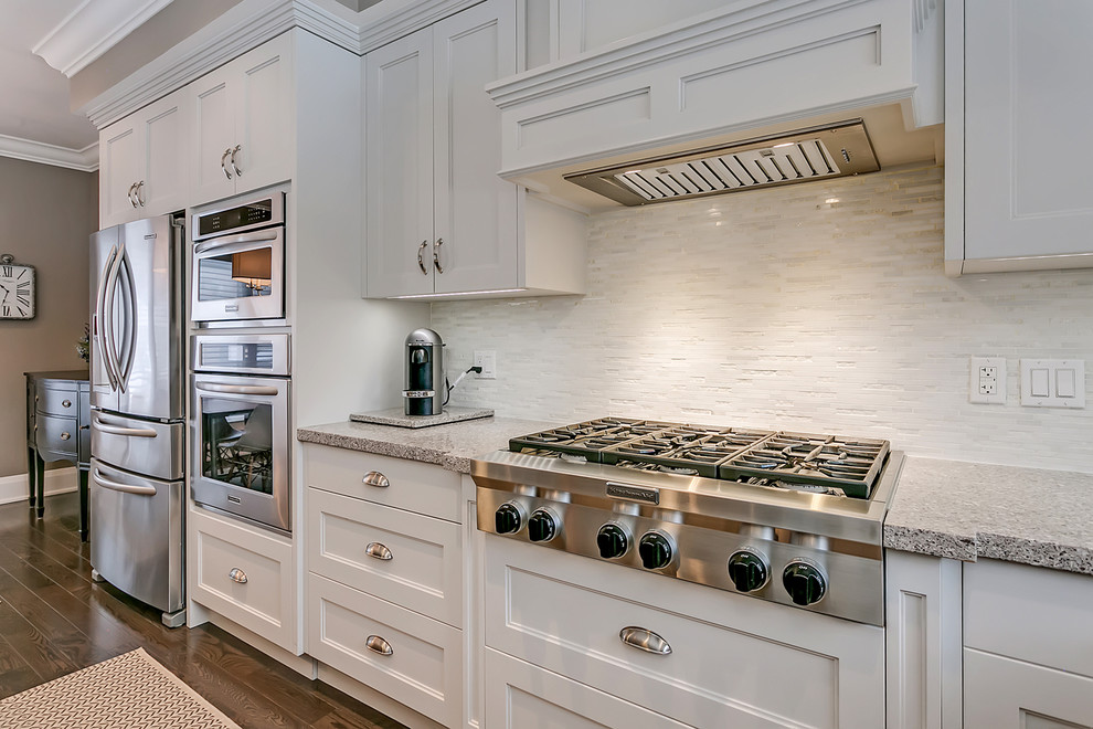 Photo of a medium sized traditional l-shaped open plan kitchen in Toronto with a submerged sink, recessed-panel cabinets, white cabinets, engineered stone countertops, white splashback, matchstick tiled splashback, stainless steel appliances, an island and multicoloured worktops.