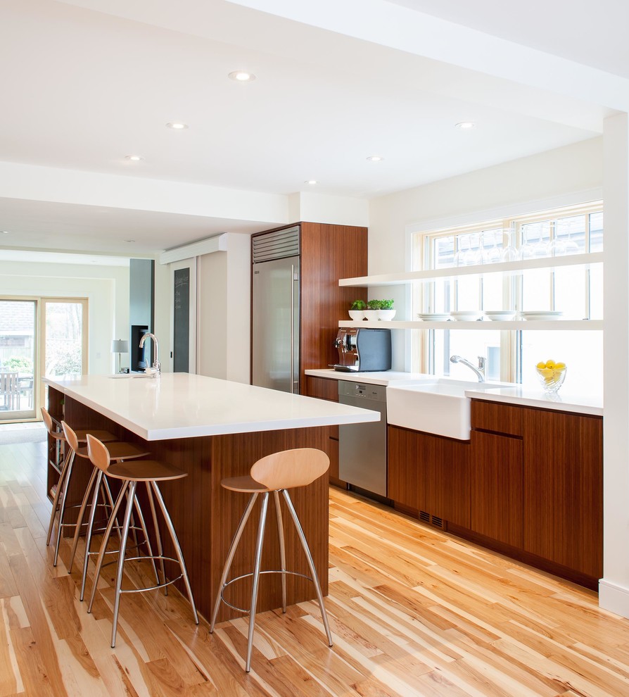 This is an example of a medium sized contemporary galley kitchen in Toronto with a belfast sink, stainless steel appliances, an island, flat-panel cabinets, dark wood cabinets and light hardwood flooring.