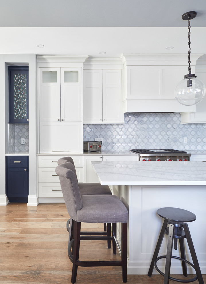 This is an example of a large classic l-shaped open plan kitchen in Toronto with a belfast sink, shaker cabinets, white cabinets, engineered stone countertops, white splashback, marble splashback, stainless steel appliances, medium hardwood flooring, an island, brown floors and multicoloured worktops.