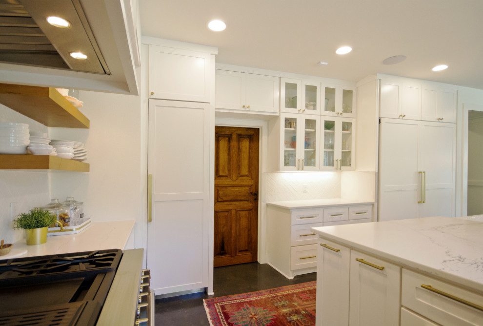 Foto på ett stort vintage vit kök, med skåp i shakerstil, vita skåp, bänkskiva i kvarts, vitt stänkskydd, stänkskydd i tegel, integrerade vitvaror, betonggolv, en köksö och grått golv