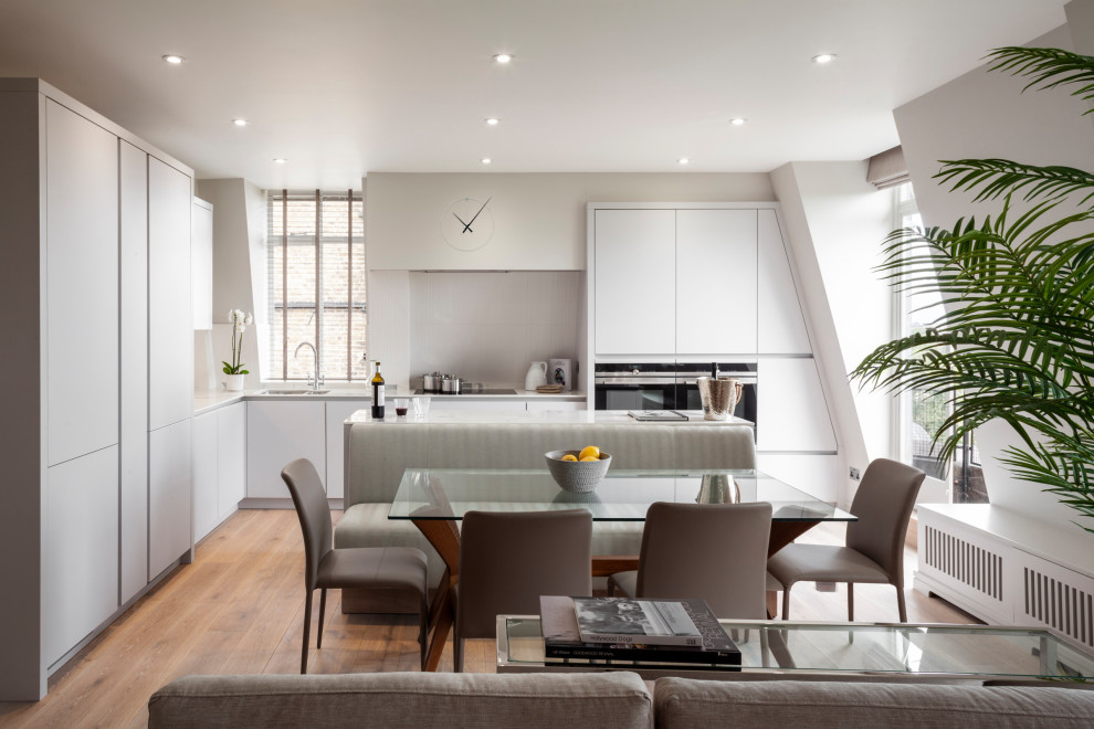 Mid-sized trendy l-shaped light wood floor and gray floor eat-in kitchen photo in London with a drop-in sink, gray cabinets, solid surface countertops, white backsplash, ceramic backsplash, stainless steel appliances, an island and white countertops