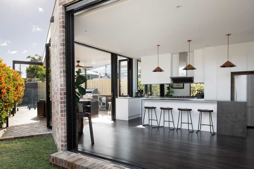 Example of a trendy galley painted wood floor and black floor open concept kitchen design in Sydney with a drop-in sink, white cabinets, solid surface countertops, mirror backsplash, stainless steel appliances, an island and gray countertops