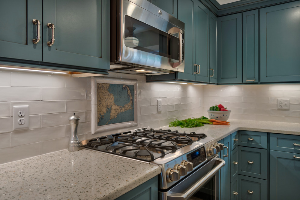This is an example of a small modern l-shaped kitchen pantry in Boston with a belfast sink, shaker cabinets, blue cabinets, recycled glass countertops, white splashback, ceramic splashback, stainless steel appliances, ceramic flooring, an island and beige floors.