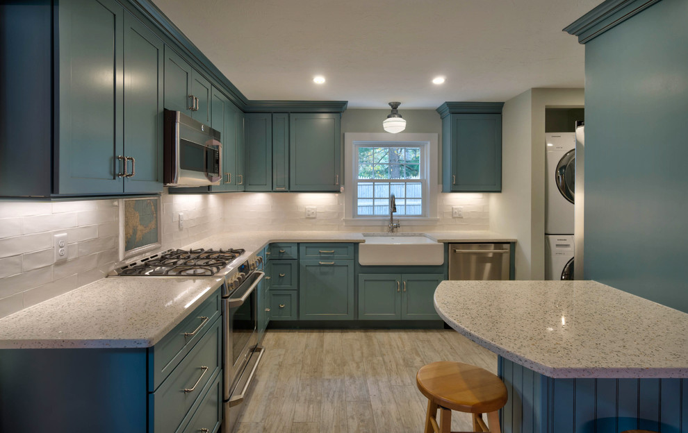 Photo of a small modern l-shaped kitchen pantry in Boston with a belfast sink, shaker cabinets, blue cabinets, recycled glass countertops, white splashback, ceramic splashback, stainless steel appliances, ceramic flooring, an island and beige floors.