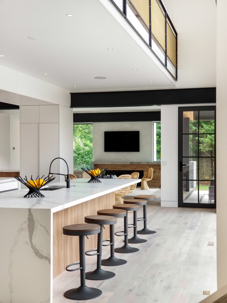 Inspiration for a large contemporary l-shaped open plan kitchen in New York with a built-in sink, flat-panel cabinets, medium wood cabinets, marble worktops, brown splashback, wood splashback, stainless steel appliances, light hardwood flooring, an island, beige floors and white worktops.