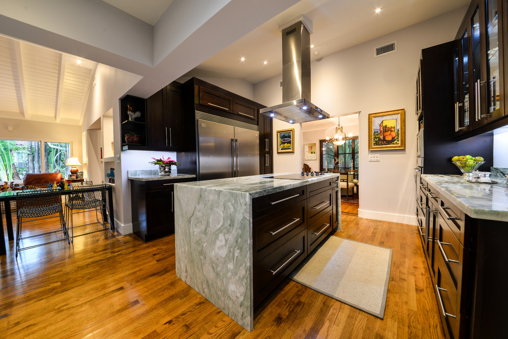 Cette image montre une grande cuisine américaine traditionnelle en U et bois foncé avec un placard à porte shaker, plan de travail en marbre, un électroménager en acier inoxydable, un sol en bois brun, îlot et un sol marron.