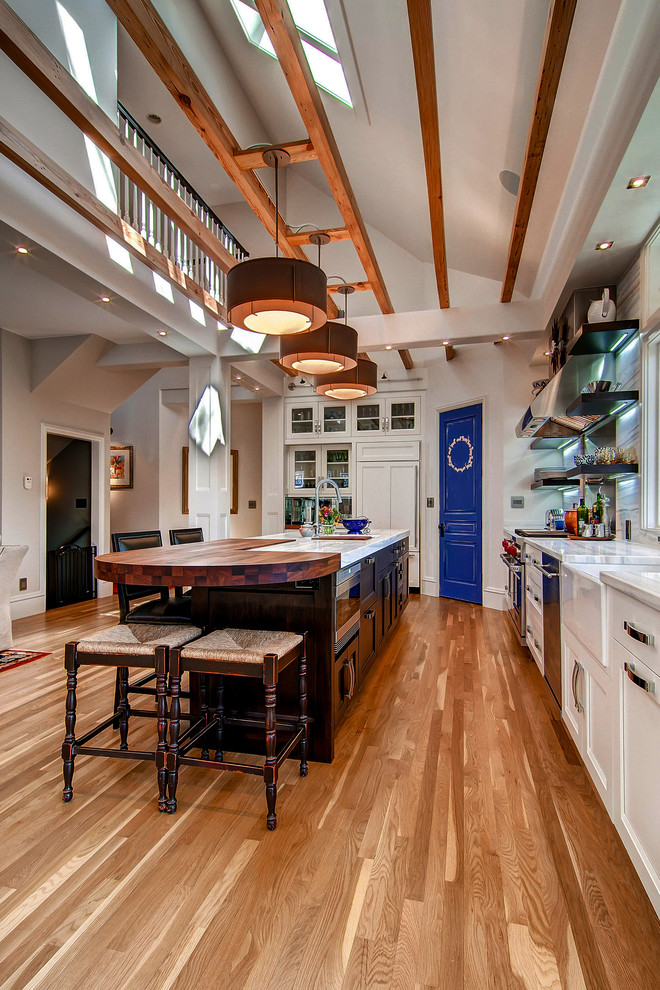 Cette photo montre une cuisine chic en L avec un placard à porte shaker, des portes de placard blanches, un électroménager en acier inoxydable, un sol en bois brun et îlot.