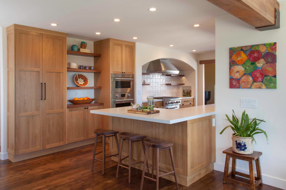 Foto på ett amerikanskt vit parallellkök, med skåp i shakerstil, skåp i mellenmörkt trä, vitt stänkskydd, rostfria vitvaror, mellanmörkt trägolv, en halv köksö och brunt golv