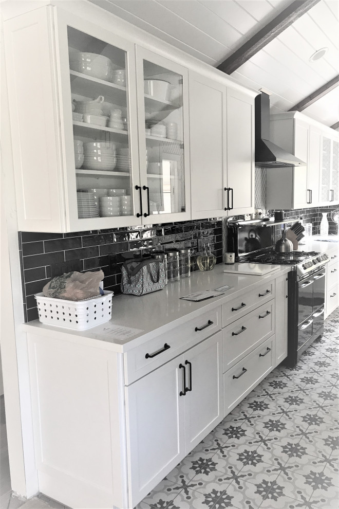 Medium sized traditional galley enclosed kitchen in Los Angeles with a belfast sink, shaker cabinets, white cabinets, engineered stone countertops, black splashback, metro tiled splashback, black appliances, cement flooring, no island, multi-coloured floors, white worktops and a vaulted ceiling.