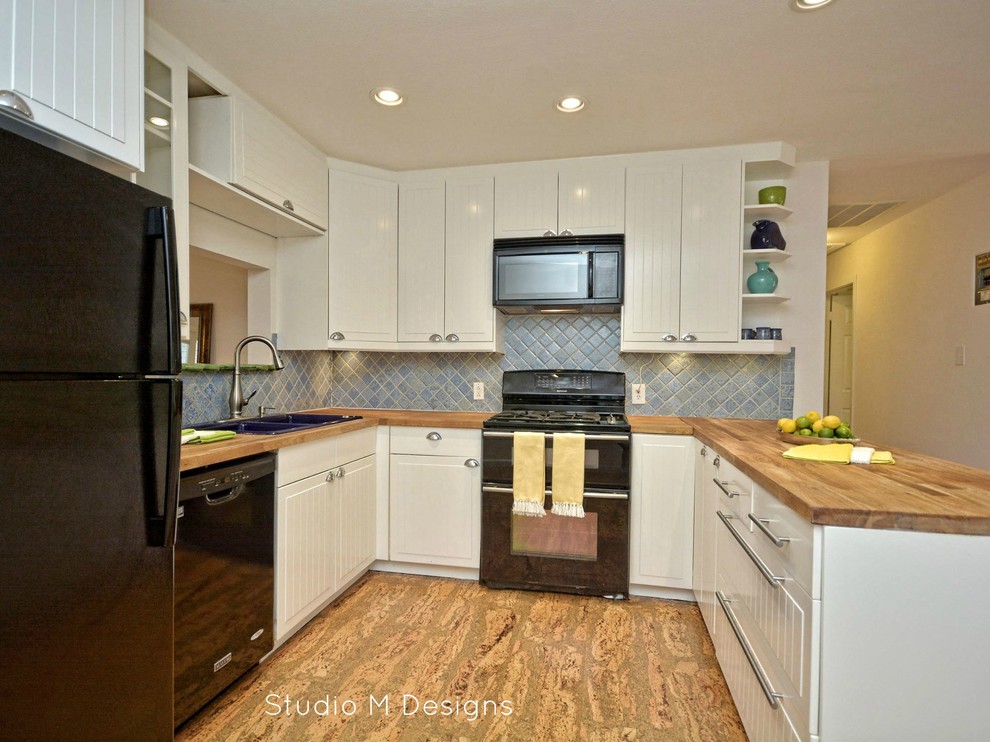 Example of a small eclectic u-shaped cork floor open concept kitchen design in Austin with a drop-in sink, beaded inset cabinets, white cabinets, wood countertops, blue backsplash, ceramic backsplash, black appliances and no island