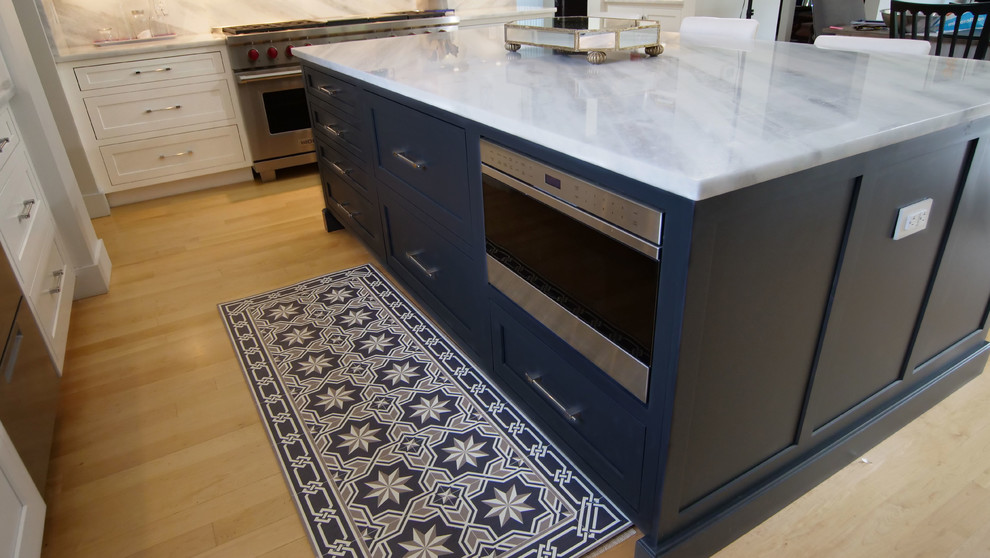 Modern inredning av ett stort vit vitt kök, med en undermonterad diskho, skåp i shakerstil, blå skåp, granitbänkskiva, vitt stänkskydd, rostfria vitvaror, ljust trägolv, en köksö och brunt golv