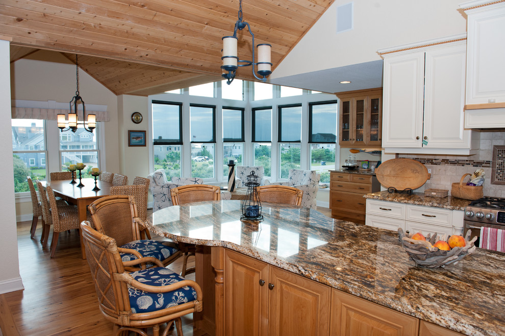 Mid-sized beach style medium tone wood floor open concept kitchen photo in Other with raised-panel cabinets, white cabinets, granite countertops, beige backsplash, stone tile backsplash, stainless steel appliances and an island