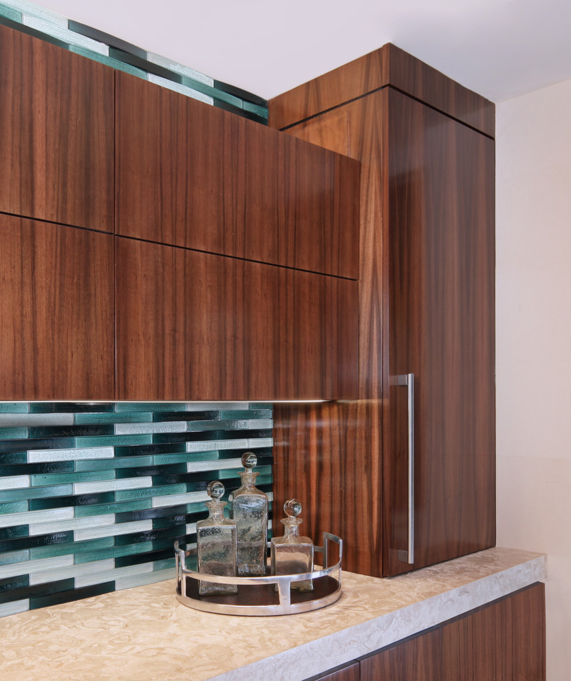 Cette image montre une cuisine ouverte parallèle design en bois foncé de taille moyenne avec un placard à porte plane, une crédence bleue, une crédence en carreau de verre, un électroménager en acier inoxydable et une péninsule.