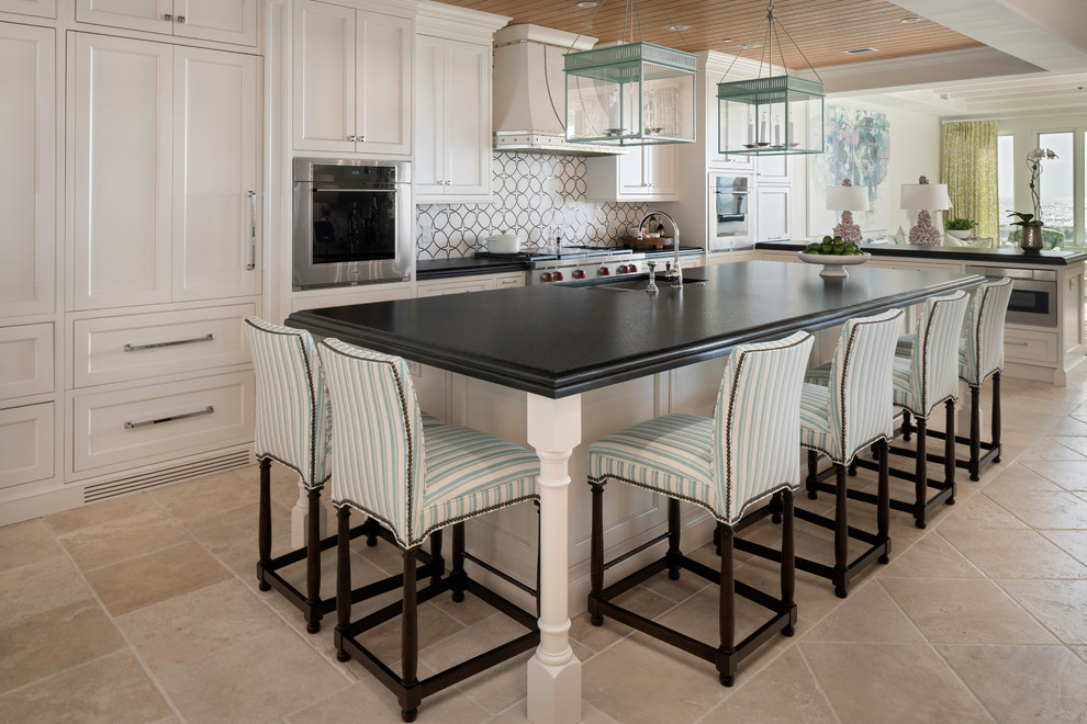 Photo of a large beach style l-shaped kitchen/diner with a built-in sink, beaded cabinets, white cabinets, white splashback, stainless steel appliances and an island.