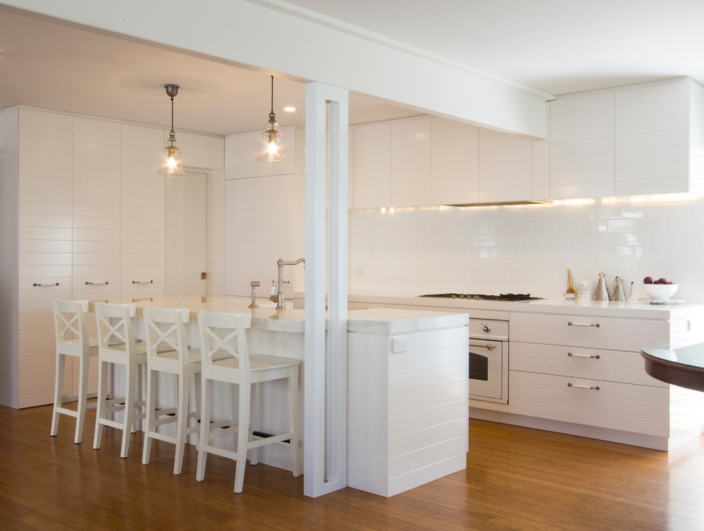 Foto på ett maritimt kök, med en köksö, vita skåp, bänkskiva i kvarts, vitt stänkskydd, stänkskydd i keramik, vita vitvaror, en rustik diskho och bambugolv
