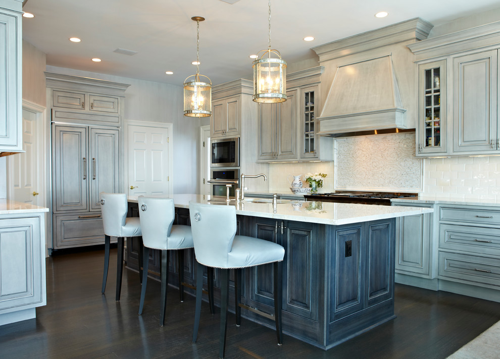Bild på ett stort kök, med luckor med upphöjd panel, integrerade vitvaror, marmorbänkskiva, vitt stänkskydd, mörkt trägolv, en undermonterad diskho, stänkskydd i tunnelbanekakel, en köksö, brunt golv och grå skåp