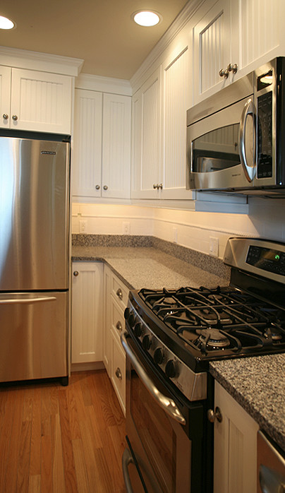 Inspiration for a contemporary u-shaped kitchen/diner in Boston with a submerged sink, shaker cabinets, white cabinets, engineered stone countertops, white splashback, ceramic splashback, stainless steel appliances, medium hardwood flooring and an island.