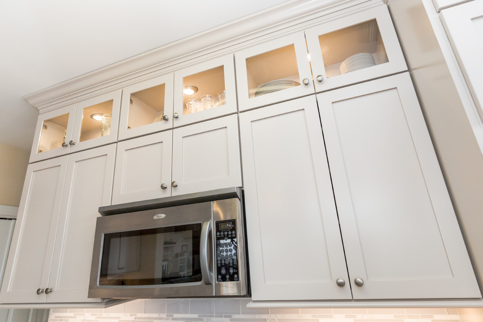This is an example of a medium sized traditional galley kitchen pantry in New York with a belfast sink, shaker cabinets, white cabinets, engineered stone countertops, white splashback, glass sheet splashback, stainless steel appliances, porcelain flooring and an island.
