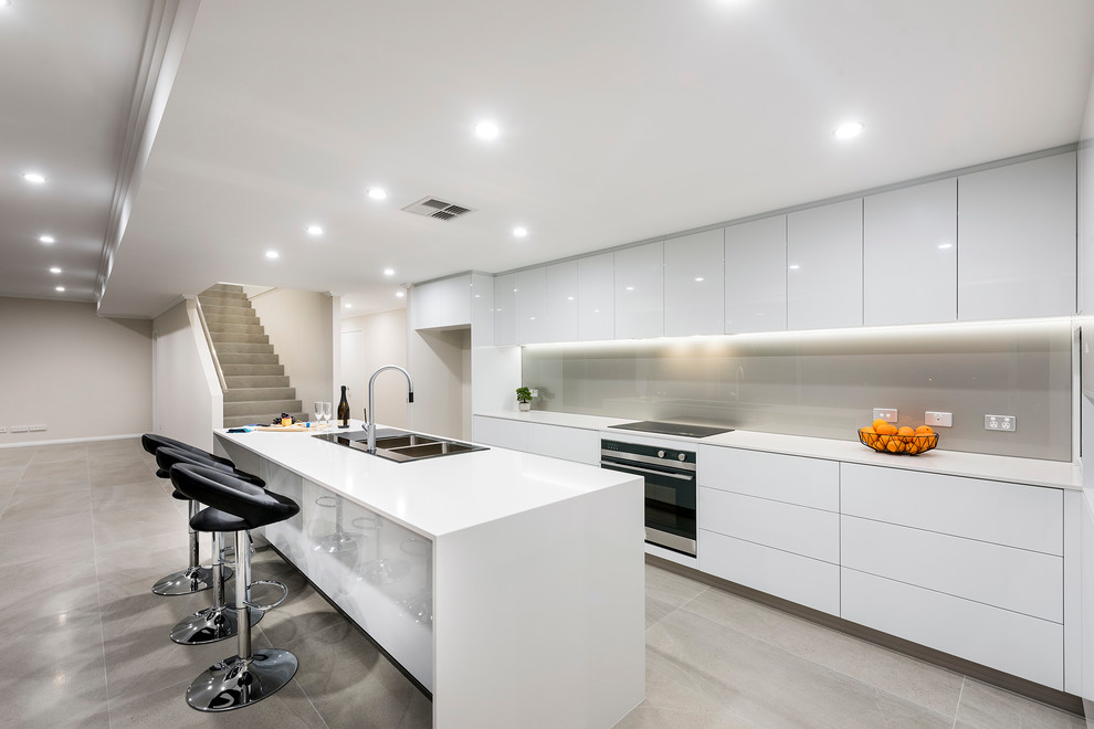 Large contemporary galley kitchen in Perth with a double-bowl sink, flat-panel cabinets, white cabinets, engineered stone countertops, an island, grey floors, white worktops, grey splashback and glass sheet splashback.
