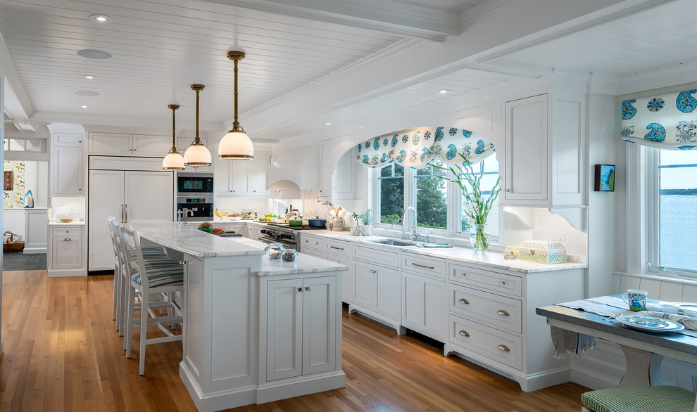 Maritim inredning av ett mycket stort kök, med en undermonterad diskho, luckor med profilerade fronter, vita skåp, marmorbänkskiva, rostfria vitvaror, ljust trägolv, en köksö och vitt golv