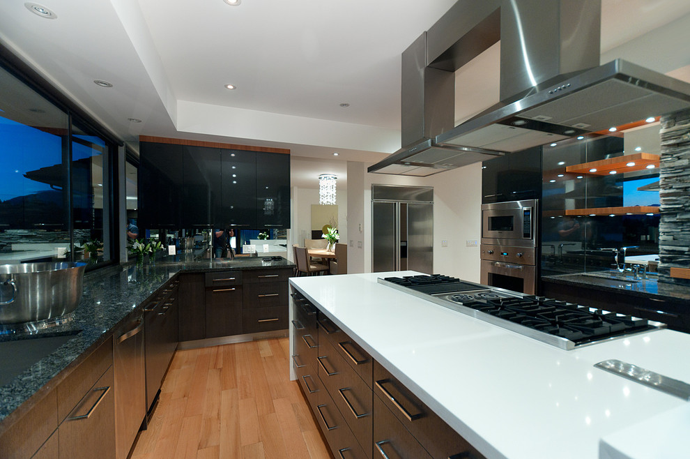 Photo of a medium sized contemporary u-shaped enclosed kitchen in Vancouver with a submerged sink, flat-panel cabinets, dark wood cabinets, marble worktops, metallic splashback, mirror splashback, stainless steel appliances, medium hardwood flooring and an island.