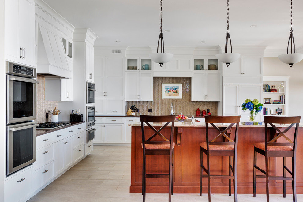 Large traditional l-shaped enclosed kitchen in Boston with white cabinets, granite worktops, glass tiled splashback, porcelain flooring, a single-bowl sink, raised-panel cabinets, metallic splashback, integrated appliances, multiple islands and beige floors.