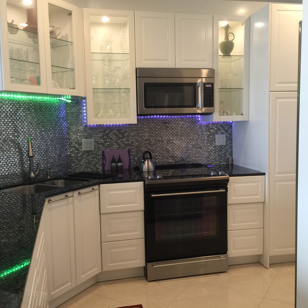 Inredning av ett modernt stort u-kök, med en undermonterad diskho, luckor med glaspanel, vita skåp, granitbänkskiva, stänkskydd i glaskakel, rostfria vitvaror, klinkergolv i porslin, en köksö och stänkskydd med metallisk yta