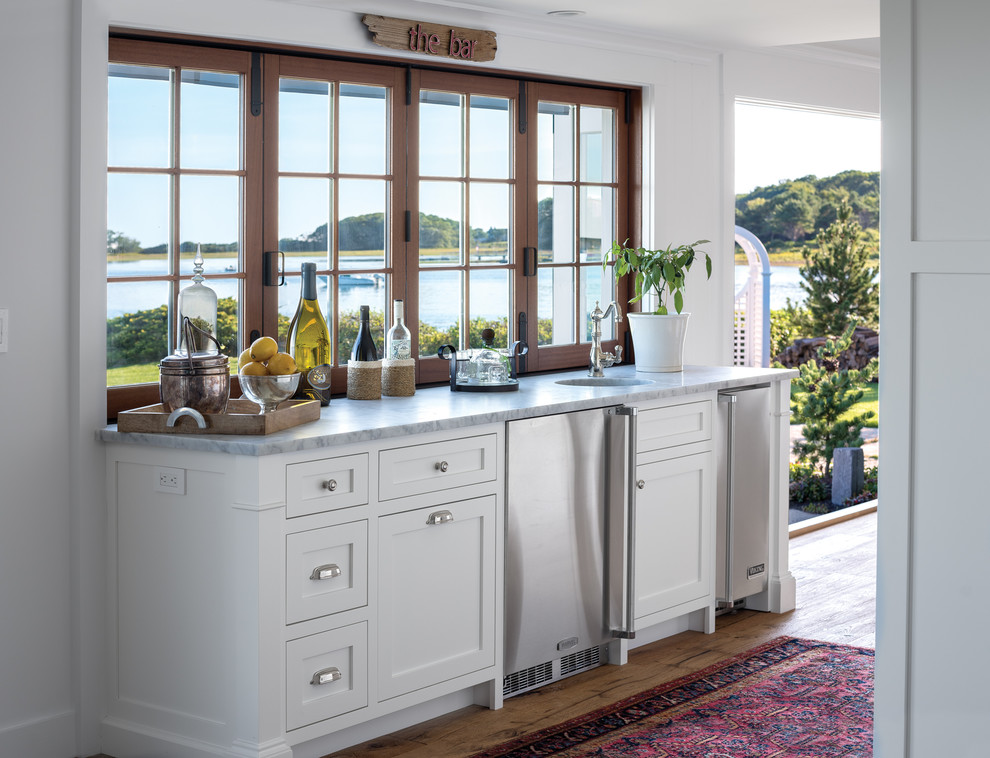 Immagine di una cucina costiera con lavello sottopiano, ante in stile shaker, ante bianche, elettrodomestici in acciaio inossidabile, parquet scuro e pavimento marrone