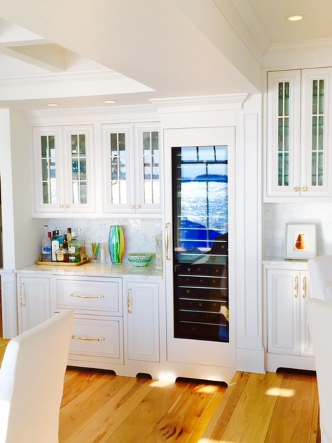 This is an example of a beach style l-shaped kitchen/diner in New York with a built-in sink, marble worktops, white splashback, stone slab splashback, stainless steel appliances, bamboo flooring and an island.