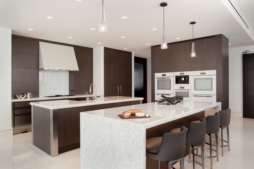 マイアミにあるラグジュアリーな広いコンテンポラリースタイルのおしゃれなマルチアイランドキッチン (フラットパネル扉のキャビネット、再生ガラスカウンター、白いキッチンパネル、白い調理設備、大理石の床、白い床、濃色木目調キャビネット、ガラス板のキッチンパネル、白いキッチンカウンター) の写真