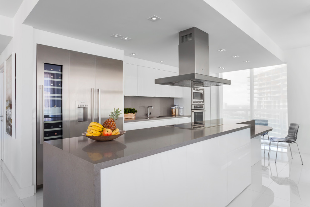 Large contemporary single-wall kitchen/diner in Miami with flat-panel cabinets, white cabinets, engineered stone countertops, grey splashback, mirror splashback and an island.