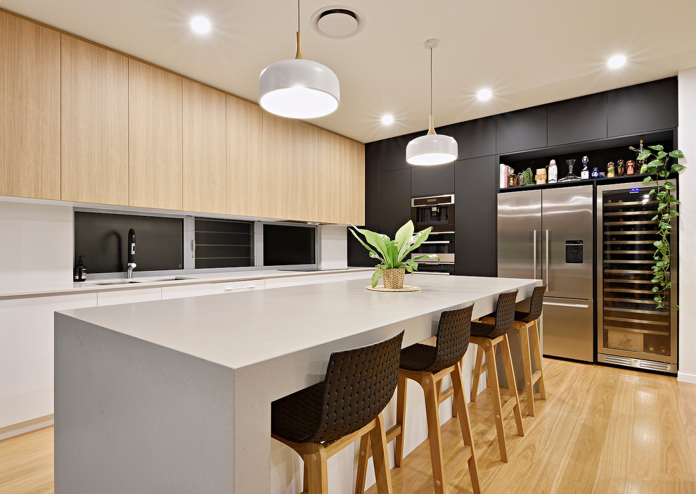 Modern inredning av ett l-kök, med släta luckor, svarta skåp, rostfria vitvaror, ljust trägolv och en köksö