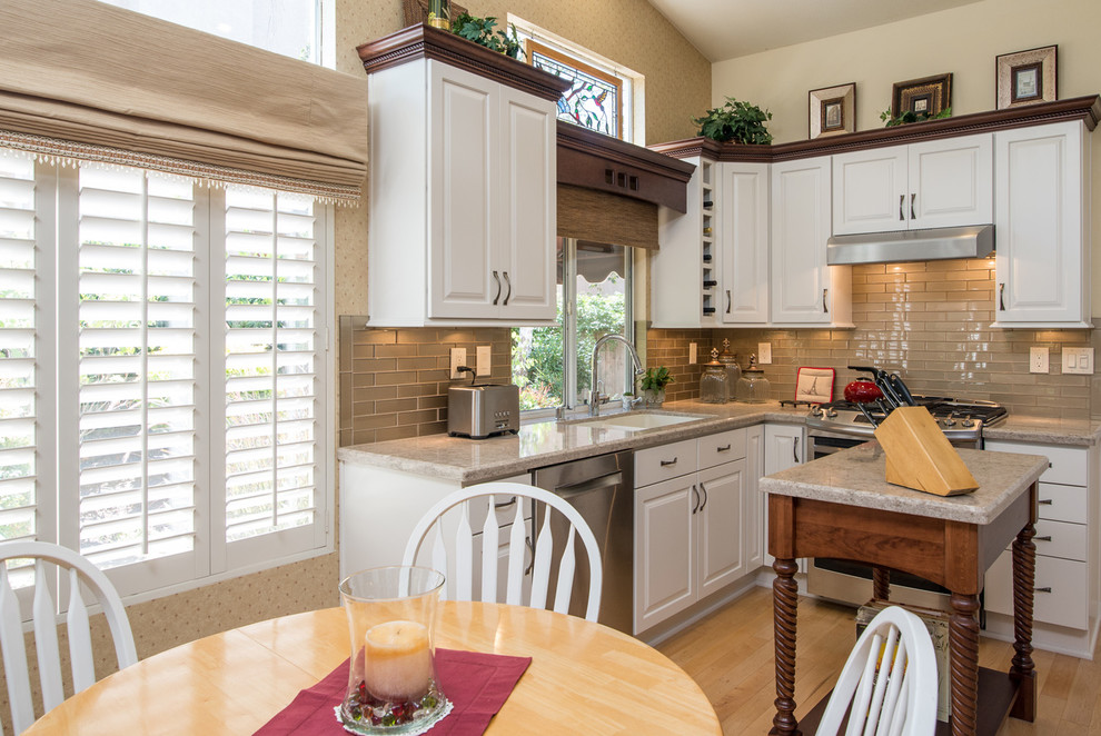 Exempel på ett mellanstort klassiskt kök, med en dubbel diskho, luckor med upphöjd panel, vita skåp, granitbänkskiva, grått stänkskydd, stänkskydd i glaskakel, rostfria vitvaror, ljust trägolv och en köksö