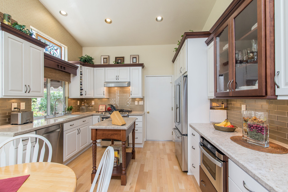 Photo of a medium sized classic u-shaped kitchen/diner in San Diego with a double-bowl sink, raised-panel cabinets, white cabinets, granite worktops, grey splashback, glass tiled splashback, stainless steel appliances, light hardwood flooring and an island.