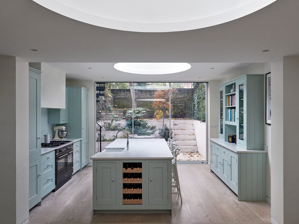 Modelo de cocina tradicional renovada de tamaño medio con fregadero sobremueble, puertas de armario azules, electrodomésticos negros, una isla, armarios estilo shaker y suelo de madera clara