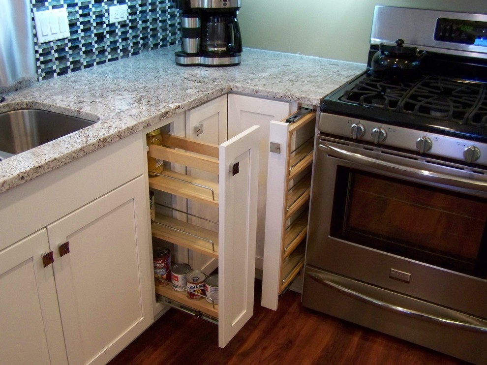 Bild på ett avskilt, litet vintage u-kök, med en undermonterad diskho, skåp i shakerstil, vita skåp, granitbänkskiva, blått stänkskydd, stänkskydd i glaskakel, rostfria vitvaror, mellanmörkt trägolv och en halv köksö