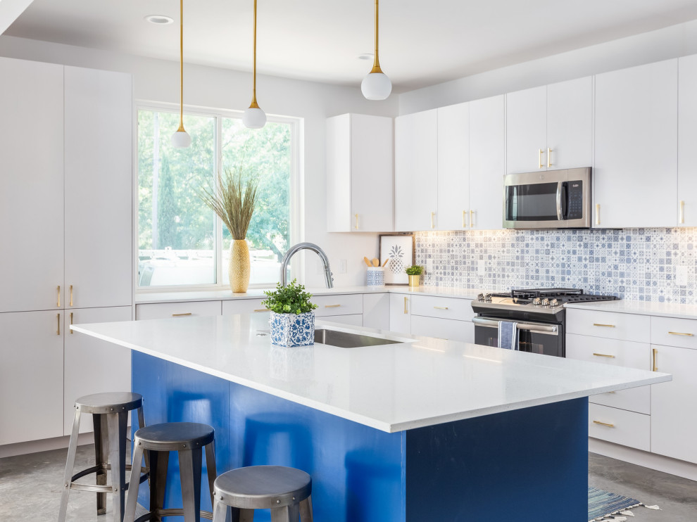 Inredning av ett modernt vit vitt l-kök, med en undermonterad diskho, släta luckor, vita skåp, blått stänkskydd, stänkskydd i mosaik, rostfria vitvaror, en köksö och grått golv