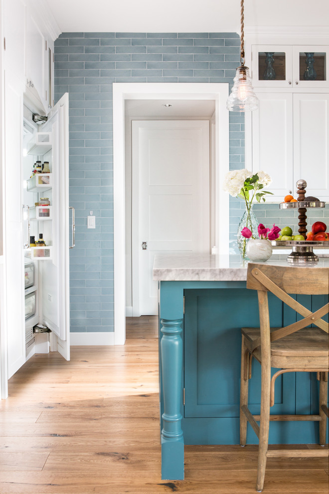 Foto de cocina tradicional renovada con armarios estilo shaker, puertas de armario azules, salpicadero azul, salpicadero de azulejos tipo metro, suelo de madera en tonos medios y una isla
