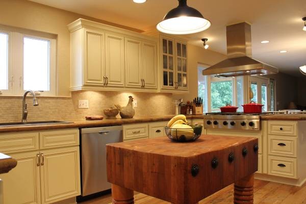 Inredning av ett klassiskt stort kök, med en undermonterad diskho, luckor med upphöjd panel, gula skåp, granitbänkskiva, beige stänkskydd, stänkskydd i keramik, rostfria vitvaror, ljust trägolv och en köksö