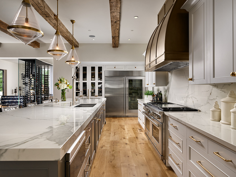 Exempel på ett klassiskt vit vitt kök, med en dubbel diskho, luckor med infälld panel, grå skåp, vitt stänkskydd, stänkskydd i sten, rostfria vitvaror, ljust trägolv och en köksö