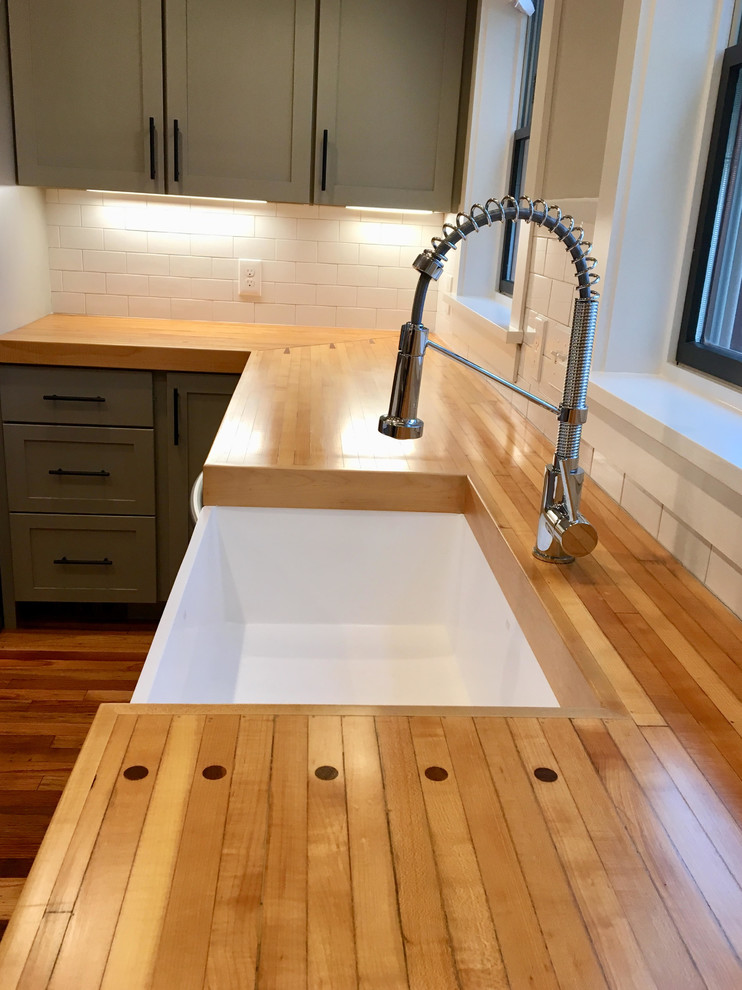 Example of a mid-sized country u-shaped medium tone wood floor and brown floor kitchen design in Cleveland with a farmhouse sink, shaker cabinets, gray cabinets, wood countertops, white backsplash, subway tile backsplash, stainless steel appliances, an island and brown countertops