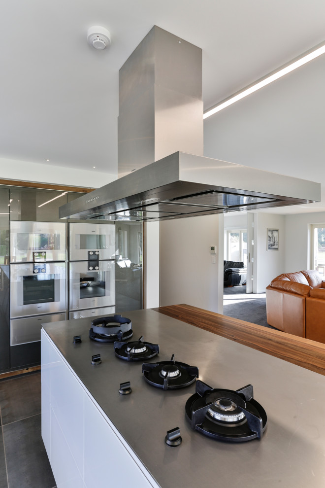 Exempel på ett mycket stort modernt linjärt kök med öppen planlösning, med en integrerad diskho, luckor med glaspanel, vita skåp, bänkskiva i rostfritt stål, grått stänkskydd, stänkskydd i porslinskakel, rostfria vitvaror, klinkergolv i porslin, en köksö och grått golv