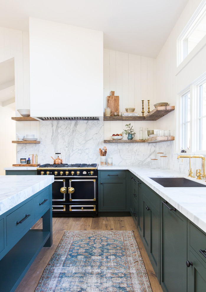 Design ideas for a nautical l-shaped kitchen in Los Angeles with a submerged sink, recessed-panel cabinets, green cabinets, grey splashback, black appliances, light hardwood flooring, an island and beige floors.