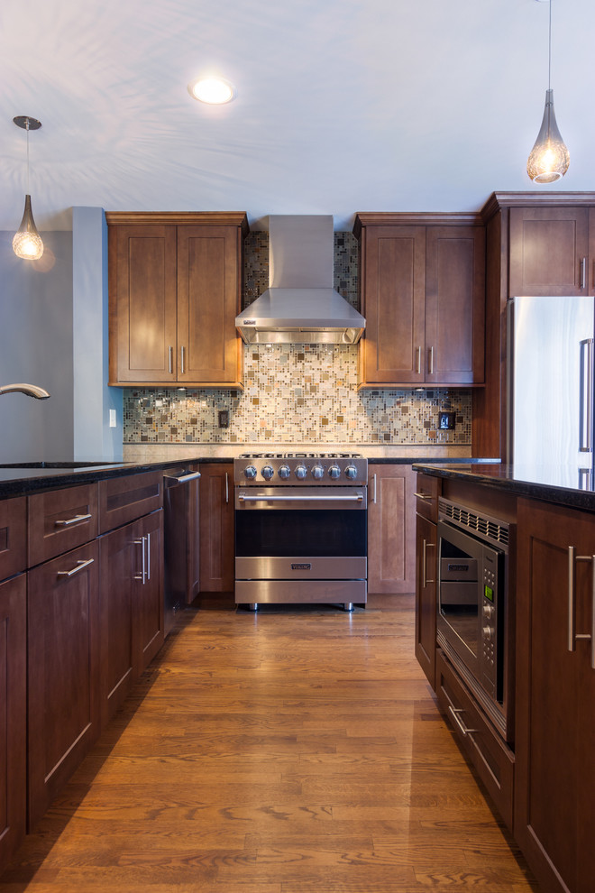 Klassisk inredning av ett mellanstort, avskilt brun brunt l-kök, med en dubbel diskho, skåp i shakerstil, skåp i mellenmörkt trä, flerfärgad stänkskydd, stänkskydd i mosaik, rostfria vitvaror, mellanmörkt trägolv, en köksö, granitbänkskiva och blått golv