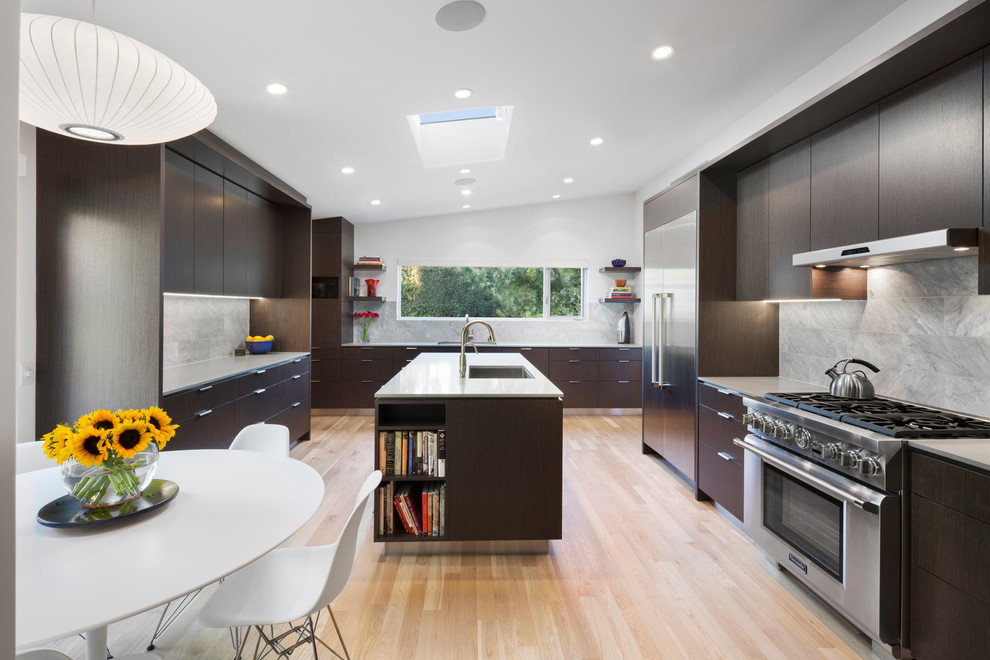 This is an example of a large contemporary u-shaped kitchen/diner in Los Angeles with dark wood cabinets, stainless steel appliances, light hardwood flooring, an island, a submerged sink, flat-panel cabinets and grey splashback.